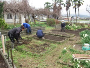 入居者による庭園菜園での農作業風景。複数名が野菜栽培に従事。